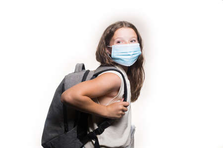 A portrait of a teenage Caucasian girl smiling, with a face mask on, holding a backpack, isolated on the white backgroundの写真素材