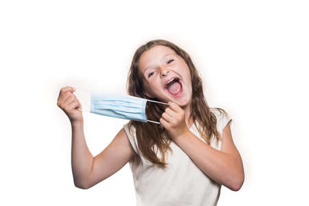 A portrait of a teenage Caucasian girl smiling, pulling the medical mask apart, holding with both hands, isolated on the white backgroundの写真素材