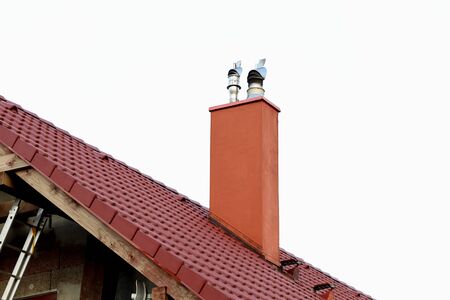 Detail of a chimney on a red classic saddle tile roof separated on a white background. Chimney with two steel pipes. Roof and chimney of family house. の写真素材