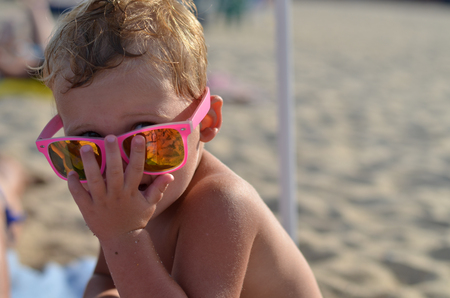 Little child wearing pink sunglasses on the beachの写真素材