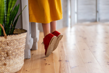 Girl in deep yellow dress is standing on tiptoe by wooden cupboard in the kitchen. Close-up burgundy childs shoes standing on light laminate floor. In handmade rustic planter green flower sansevieriaの写真素材
