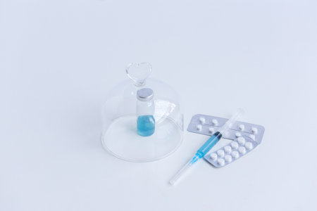 On white isolated background lie a syringe with medicine, a vial with a blue vaccine against viruses, pills for flu, colds. Medical preparations for the fight against the epidemic. Mock up, copy spaceの写真素材