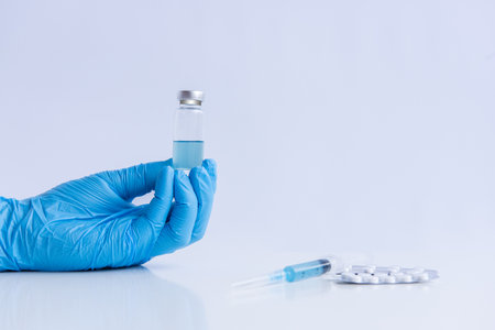 On white isolated background, hands of doctor in medical blue gloves hold ampoule vaccine against virus coronovirus. Syringe with antidote, pain pills. Fighting pandemic, epidemic. Mock up, copy spaceの写真素材