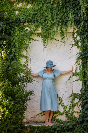 Portrait of middle aged pregnant woman in denim blue dress, hat. Future mother stands near antique ruins, grunge background green ivy. Travel during pregnancy. Maternity, pregnancy concept. Copy spaceの写真素材