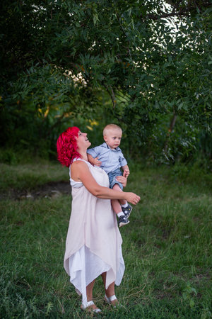 Portrait of bright, diversity, extraordinary mother and little son embrace in the forest. Woman has pink hair. Tender motherhood, happy childhood. Rest, walk in nature in the countryside. Copy spaceの写真素材