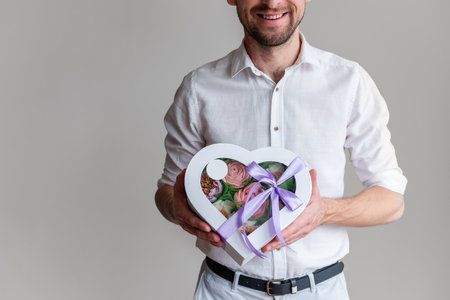 Faceless man holds box shape of heart of marshmallow sweet flowers in hands. Gift with purple ribbon. Delicate sugarless roses on light background. Small business at home. Hobby baking. Holiday giftの写真素材