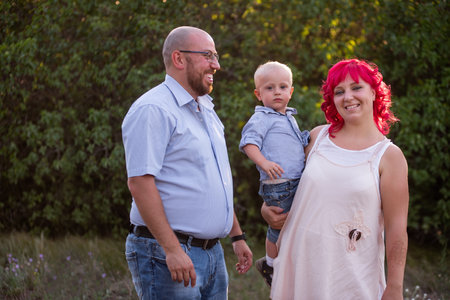Bald father in glasses looks lovingly at wife with pink hair and son in blue shirt. Close-up portrait diversity family. Children Protection Day. Care of parents of one child. Copy space. Travel forestの写真素材