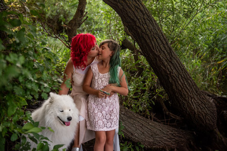In the Green Forest, by small diversity stream, mother with pink hair embrace daughter. The white fluffy samoyed guards the family. Traveling with pets on the weekend. The concept of unity with natureの写真素材