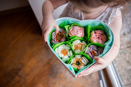 Top view close up portrait Little curly girl holds heart shaped box with homemade, sweet marshmallows in hands. Eco natural homemade products without sugar. Edible gift for the holiday. Lifestyleの写真素材