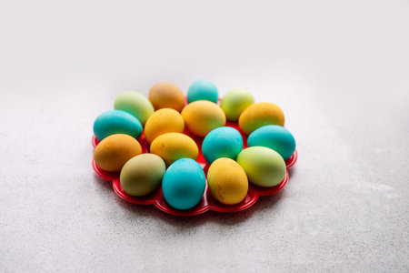 Bright Easter eggs lie on a red, round stand on a marble table. Homogeneous lifestyle background....