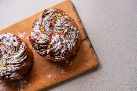 Easter Kraffin on light wooden background. Cake with candied fruits, raisins, chocolate, nuts, topping with powdered sugar, edible decorations. Rustic style baking, serving. Copy space, mock upの写真素材