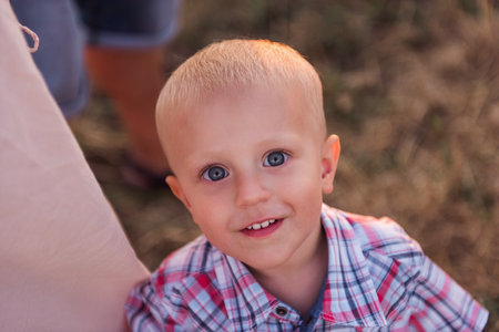 Close-up portrait of little boy in plaid shirt, hugging mothers leg. Top view of smiling toddler with blue eyes. The concept of parental protection, trust. Copy space. Cheerful childhoodの写真素材