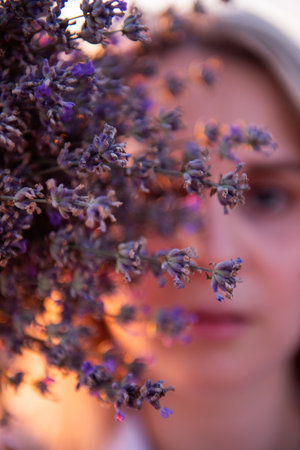 Sprigs purple lavender against background of blurred face of young blonde woman. Close-up portrait of millennial girl with clean skin without makeup. Allergy concept. Aroma oils, perfumery from natureの写真素材
