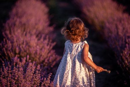 Defocused blurred little girl in flower dress stands with back in field of purple lavender among the rows at sunset. Faceless toddler child have fun on walk in countryside. Allergy concept. Copy spaceの写真素材