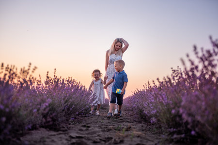 Little son daughter play catch up around mother in rows of purple lavender field. Cute, cheerful boy girl having fun in the countryside with a young woman. Weekend travel. View from below. Copy spaceの写真素材