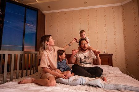 Funny portrait of diverse cheerful family on bed in morning. Stylish mother hugs daughter, father...