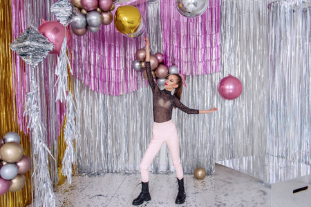 Dancing crazy Fashion girl with beauty makeup, in soft pink pants, mesh bodysuit among confetti, silver shiny foil tinsel. Models having fun with glitter balloons. New Year party. Masquerade partyの写真素材