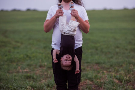Diversity father holding little son upside down playfully indicates his joyous child. Young man with...