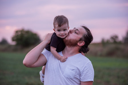Heartwarming scene of diversity father carrying smiling son on shoulders at twilight, showcasing...