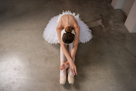 Young ballerina in ballet pointe, white tutu, tiara in serene stretch, bowing forward while seated on floor contrasting with the softness of attire. Faceless girlの写真素材