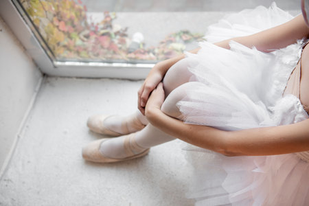 Close up ballet pointe shoes. Ballerina dancer sits by the window, pose relaxed, with pointe shoes on and the soft tulle of tutu, evoking moment of tranquility.の写真素材