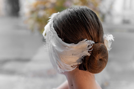 Close-up of unique white feather headband tiara wrapped around a ballerina girls hair bun, blending tradition with modern style. Ballet hairstyleの写真素材