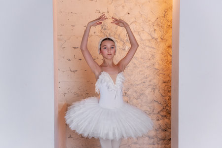 Poised young ballerina stands en pointe in hallway arch with warm garlands of lamps, elegant costume and focused demeanor embodying the spirit of classical ballet.の写真素材