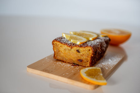 Moist homemade orange cake with raisins, garnished with fresh orange slices and powdered sugar, sits...