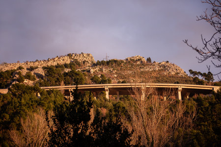 Modern highway bridge stretches across a rugged mountain landscape, surrounded by lush greenery and rocky terrain, bathed in warm golden light in Solin, Croatia.の写真素材
