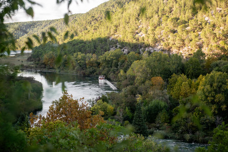 Tranquil scene in Krka national park, Croatia, featuring a tourist boat resting on the serene Krka river, surrounded by lush green trees and gentle water flowの写真素材