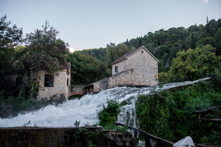 White water cascading over rocks around an old stone mill building in Krka national park, Croatia, creating a picturesque scene of nature and historyの写真素材