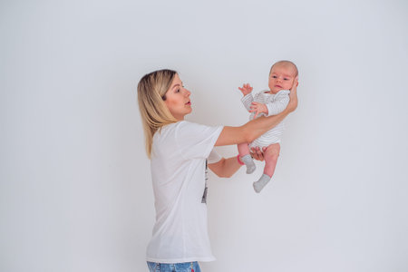 Mother lovingly holds her newborn baby in a minimalist setting. The baby wears a striped outfit,...