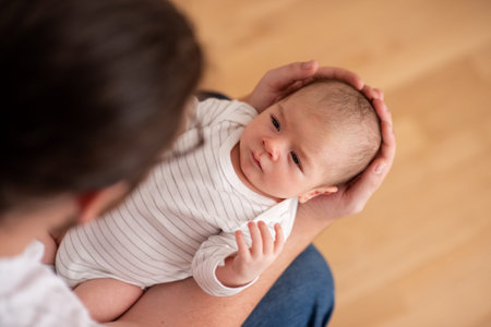 From a top view, a father tenderly cradles his newborn baby, supporting its head and body with his...