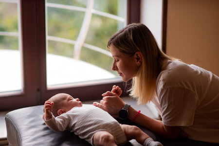 Loving mother caring for her newborn baby, gently holding his tiny hands while he rests on a...