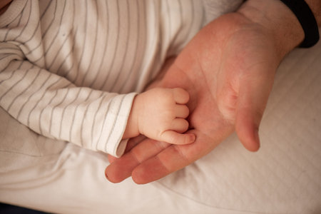 Close-up of a newborn baby's hand gently grasping its father's finger, highlighting the bond between parent and child in a tender moment of affection and careの写真素材