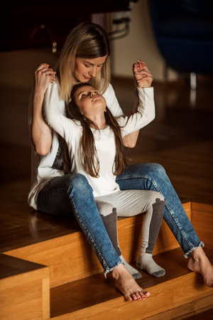 Mother lovingly holds her daughter's hands while sitting on wooden steps. The scene captures a moment of connection and support, highlighting the warmth and closeness of their relationshipの写真素材