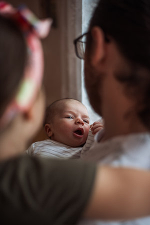 Adorable newborn baby yawning and stretching while nestled in the loving embrace of parents, capturing a tender moment filled with warmth and connection during early parenthoodの写真素材