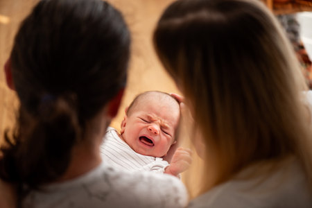 Newborn baby cries while being gently held by two parents, creating an intimate family moment. The warm lighting and soft focus emphasize the tender care and love in the sceneの写真素材