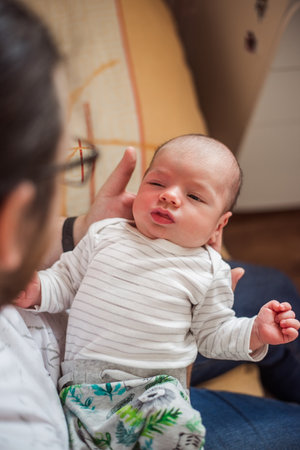 Father holding his newborn baby son, gently supporting his head and body while sitting comfortably on a sofa at home, creating a tender moment filled with love and connectionの写真素材