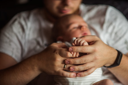 Father holding the tiny hand of his sleeping newborn baby, embodying love, care, and protection in a...