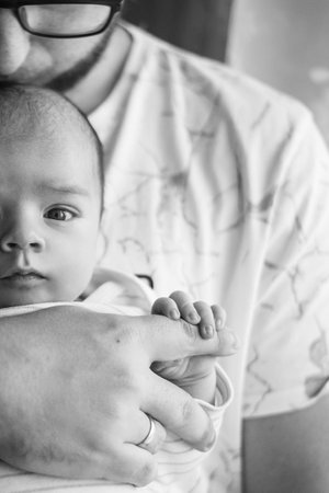 Close-up portrait of a loving father gently holding the tiny hand of his newborn baby, creating a heartwarming moment of connection and tenderness in monochromeの写真素材