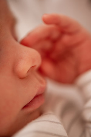 Close-up of a newborn baby sleeping peacefully, with their small hand gently resting near their...