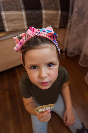 Little girl wearing a pink headband, sitting on the floor of her cozy bedroom, holding a wooden comb and looking up with curiosity and joy, embodying childhood innocence and playfulnessの写真素材