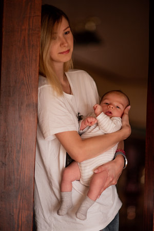 Young mother gently cradles her newborn baby in a warm, cozy home setting. The intimate moment captures the bond and tenderness between mother and child, highlighting early parenthoodの写真素材
