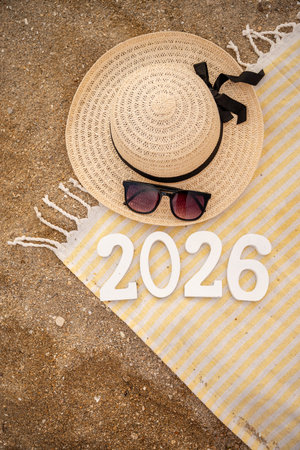 Stylish beach accessories like a straw hat, sunglasses, and a striped towel rest on sandy shores,...