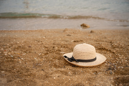 Summer vacation straw hat resting on the warm beach sand, with the sparkling sea in the background, creating a perfect scene for enjoying relaxing summer holidaysの写真素材