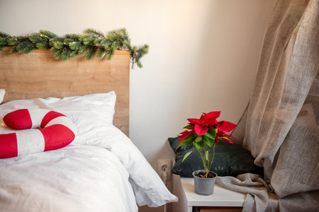 Christmas spirit filling the bedroom, featuring a vibrant poinsettia, a whimsical candy cane pillow, and a festive garland draping elegantly from the headboardの写真素材