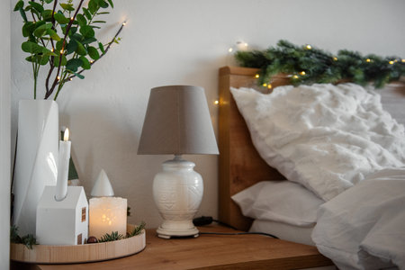 Christmas interion with decorations candles, decorative houses and fairy lights illuminating bedroom, creating cozy winter atmosphere next to comfortable bedの写真素材