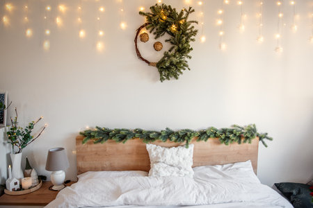 Christmas wreath and garland hanging above bed with fairy lights illuminating a cozy bedroom, creating a festive and warm atmosphere for the holiday seasonの写真素材
