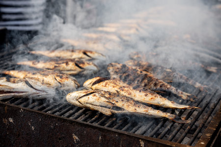 Whole fish grilling over glowing charcoal, smoke curling up as flames kiss the skin, rustic outdoor...